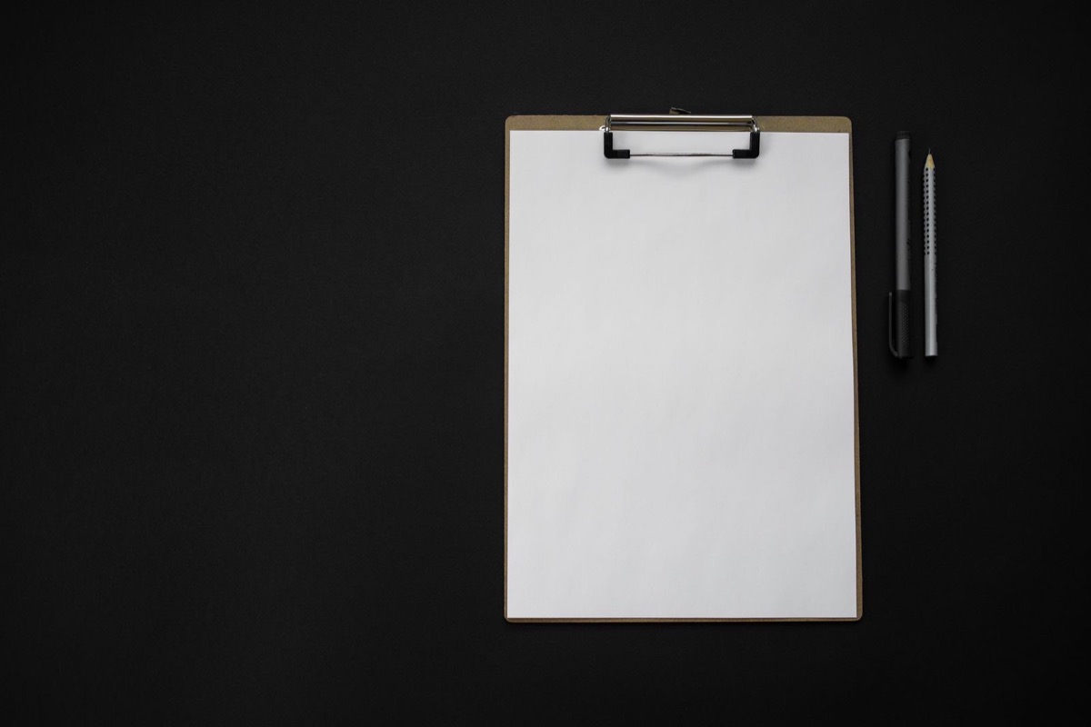 A blank clipboard and pens on a dark desk