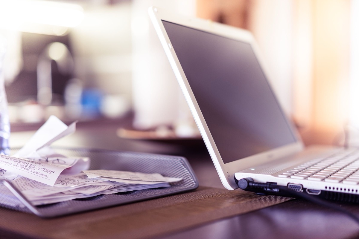 A laptop beside printed invoices and paper documents on an office desk