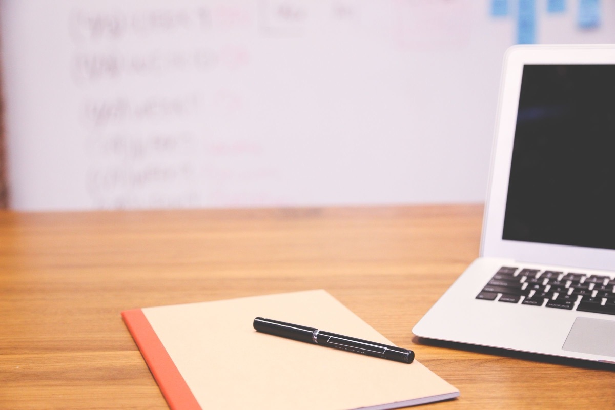 A laptop, a notebook and a pen on a desk